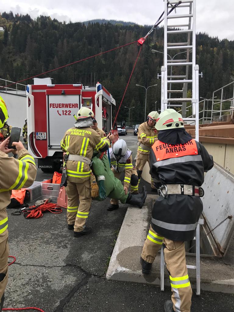 Einsatzkräfte der Feuerwehr Anras bergen mit Leiter und Seilzug eine Übungspuppe über die Beckenkante; im Hintergrund das Löschfahrzeug.