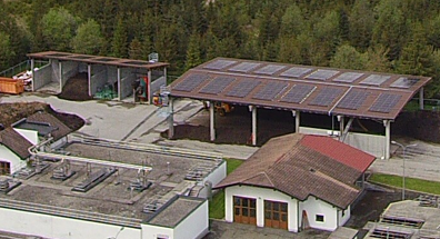 Luftbild des Klärwerksgeländes in Anras: auf dem langen Dach der offenen Kompostierhalle liegen dunkle Photovoltaikmodule, davor die Becken der Kläranlage.